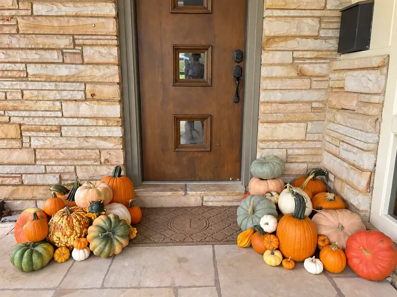 Cozy Welcome pumpkins arranged at a wood door and stone entry